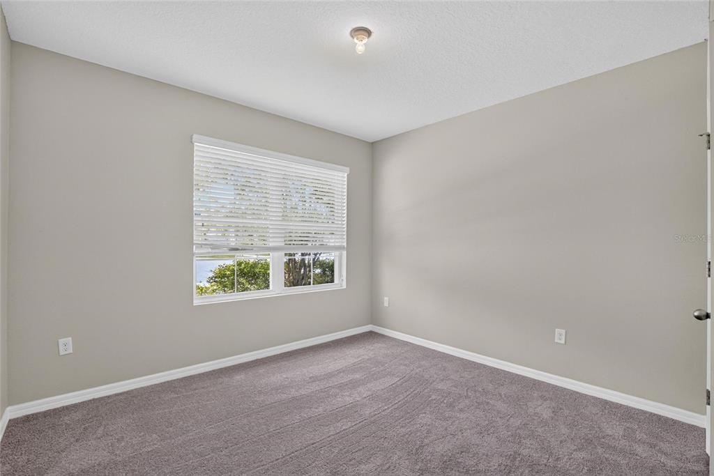An empty bedroom features neutral walls, gray carpeting, a window with blinds, and a ceiling light — 16441 TREASURE POINT DRIVE, WIMAUMA, FL