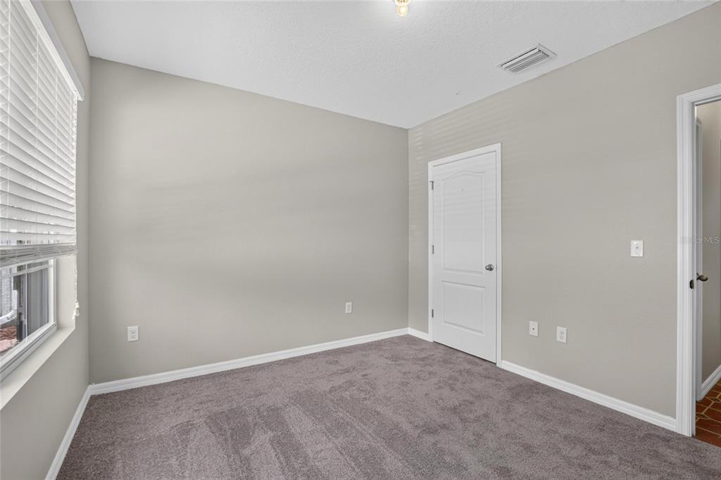An empty bedroom with gray walls, gray carpet, a window with blinds, and two doors — 16441 TREASURE POINT DRIVE, WIMAUMA, FL