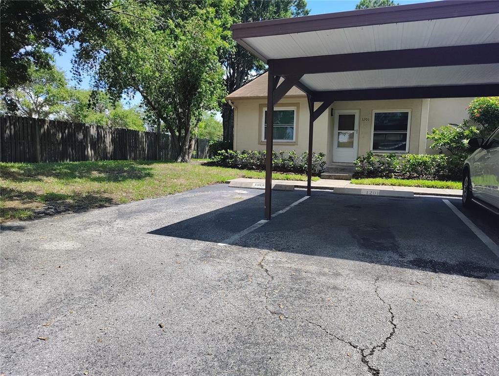 A beige house exterior features a covered carport and a paved driveway with parking spaces — 10853 43RD STREET N UNIT 1201, CLEARWATER, FL