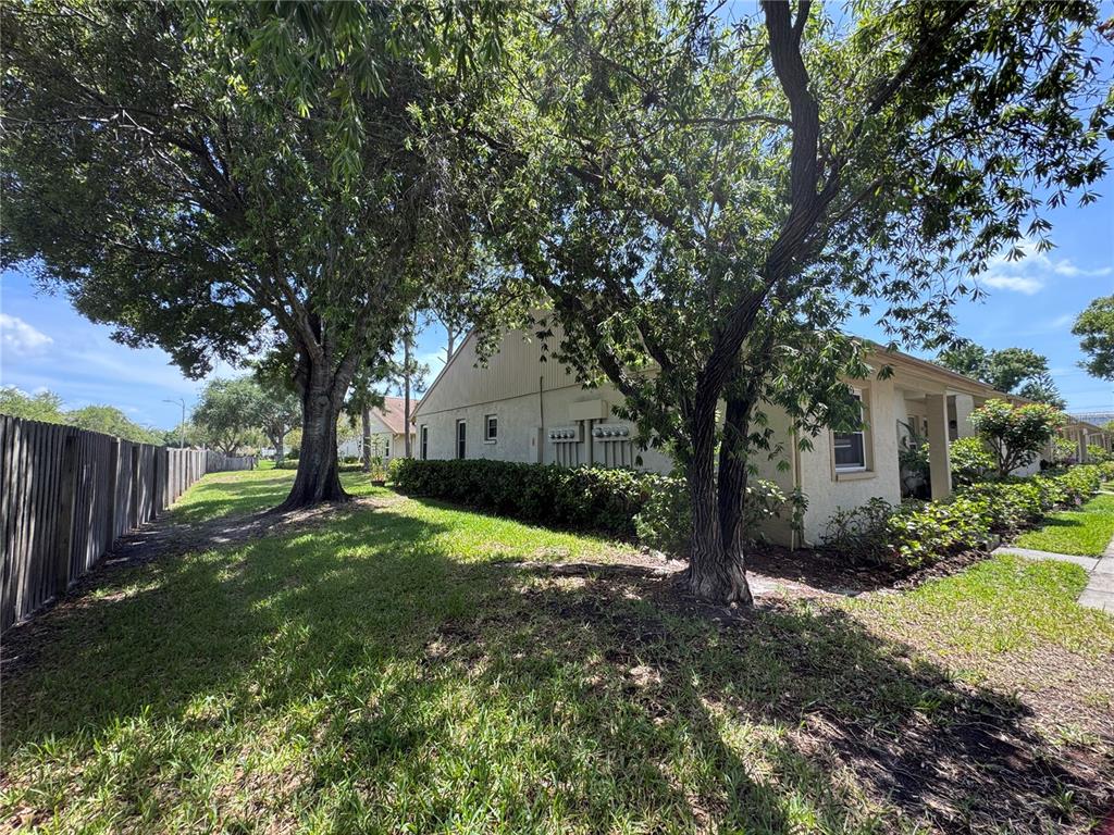 A side view of a residential building with trees, a wooden fence, and landscaping — 10853 43RD STREET N UNIT 1201, CLEARWATER, FL