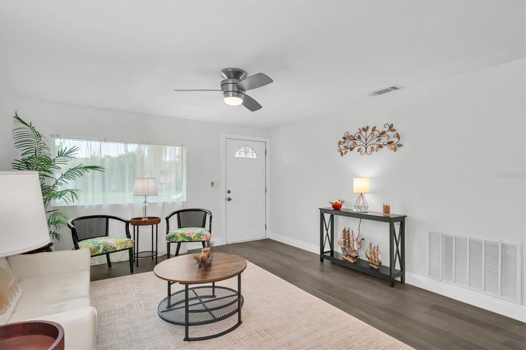 A living room features white walls, dark wood-look flooring, a ceiling fan, and a front door — 650 TIMBER BAY CIRCLE W, OLDSMAR, FL