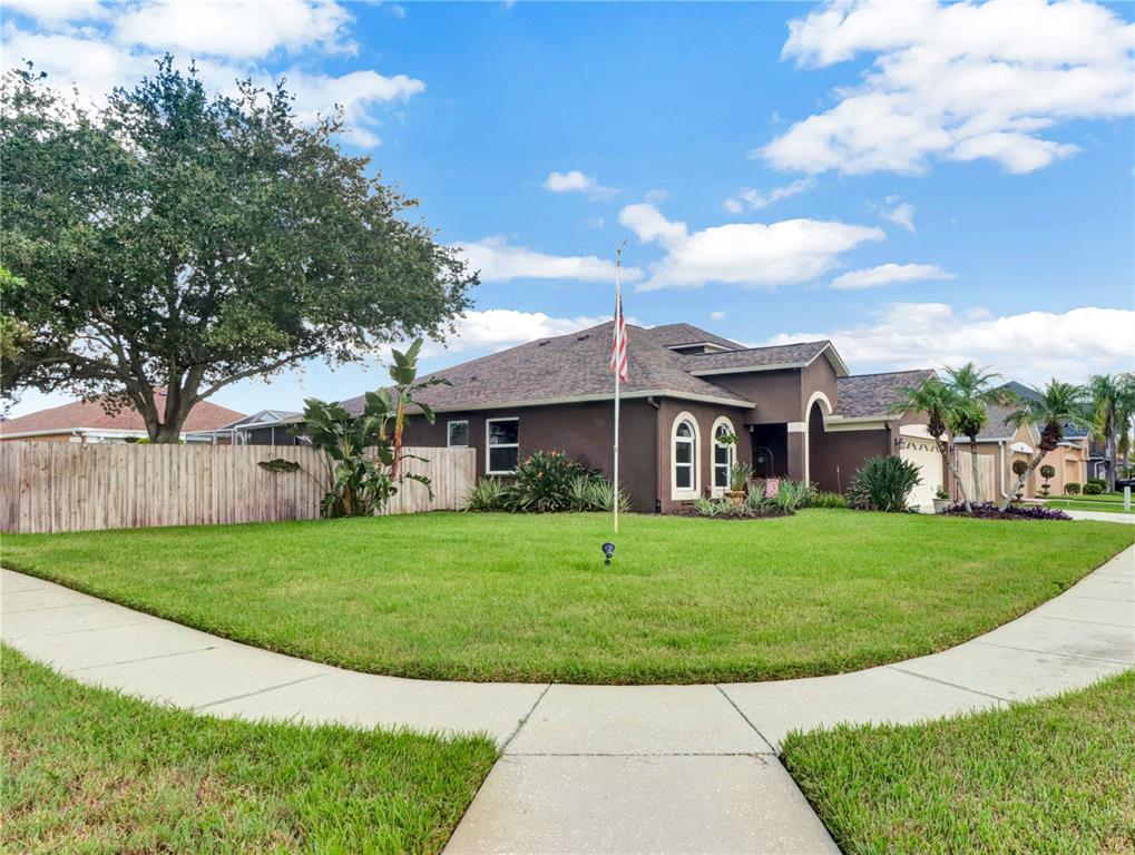 A brown single-story house with a large front lawn and a flagpole stands on a corner — 2002 RAIN DANCE PLACE, BRANDON, FL