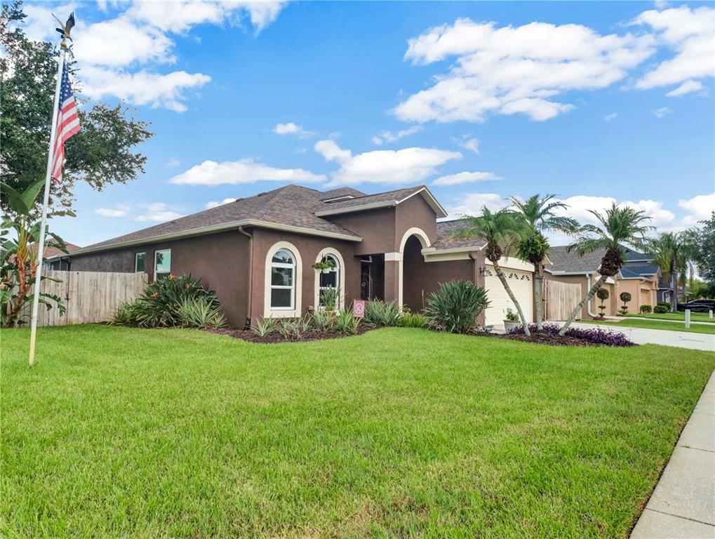 A brown single-story house with a flag pole and palm trees in the front yard — 2002 RAIN DANCE PLACE, BRANDON, FL
