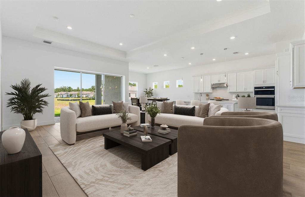 A bright, open-concept living room features two sofas, dark coffee tables, and a modern kitchen — 16412 RUSTIC SKY DRIVE, SPRING HILL, FL
