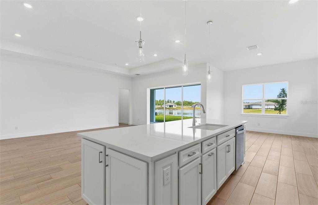 A kitchen island with a sink sits in a bright room with light wood flooring — 16412 RUSTIC SKY DRIVE, SPRING HILL, FL
