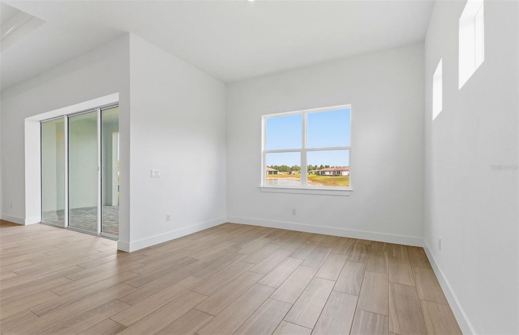 An empty room features light wood-look tile flooring, white walls, and a sliding glass door — 16412 RUSTIC SKY DRIVE, SPRING HILL, FL
