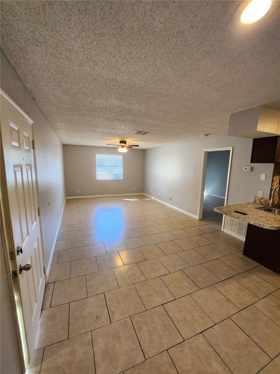 An open-concept living area features light-colored tile flooring, a ceiling fan, and a kitchen counter — 245 RED MAPLE PLACE, BRANDON, FL