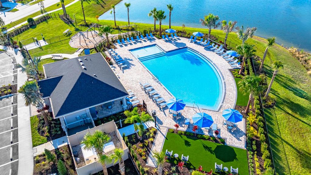 An aerial view shows a community swimming pool, clubhouse, playground, and lake in a neighborhood — 860 STEEL DRIVE, APOLLO BEACH, FL