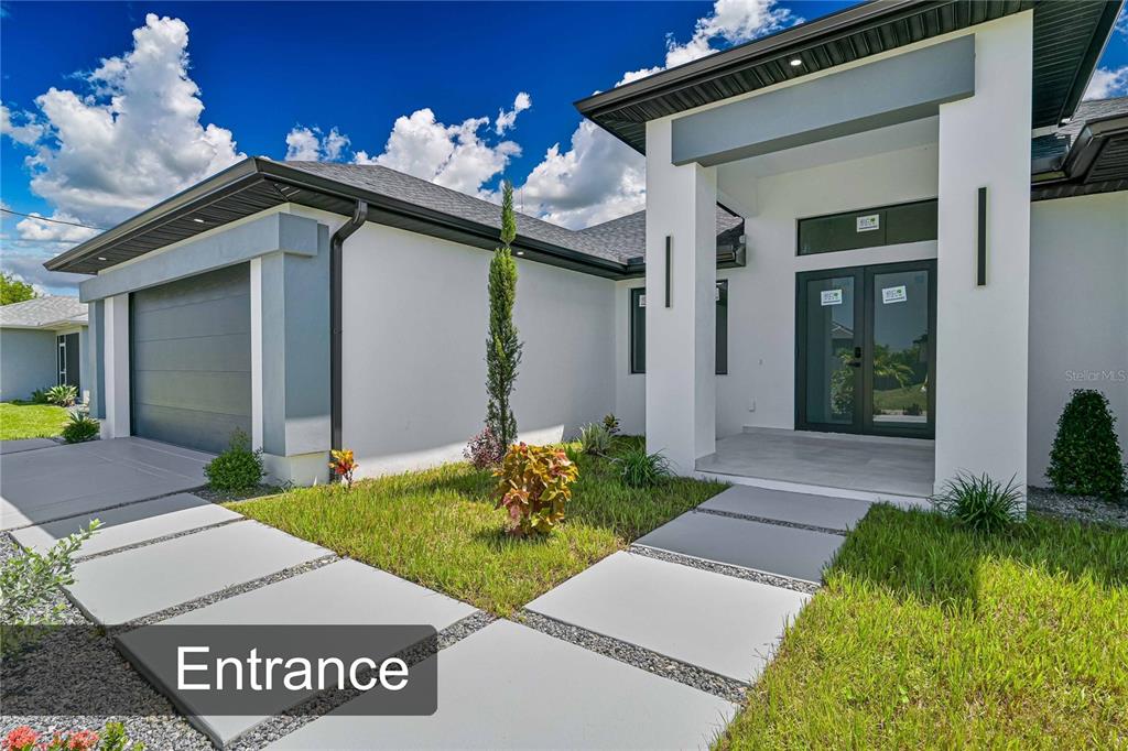 A modern single-story house exterior features a gray garage, white stucco walls, and a paved walkway — 425 SW 31ST AVENUE, CAPE CORAL, FL