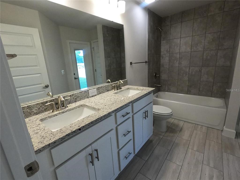 A bathroom features a double vanity with granite countertops, white cabinetry, and a tiled tub-shower — 36861 HIDDEN VIEW CIRCLE, DADE CITY, FL