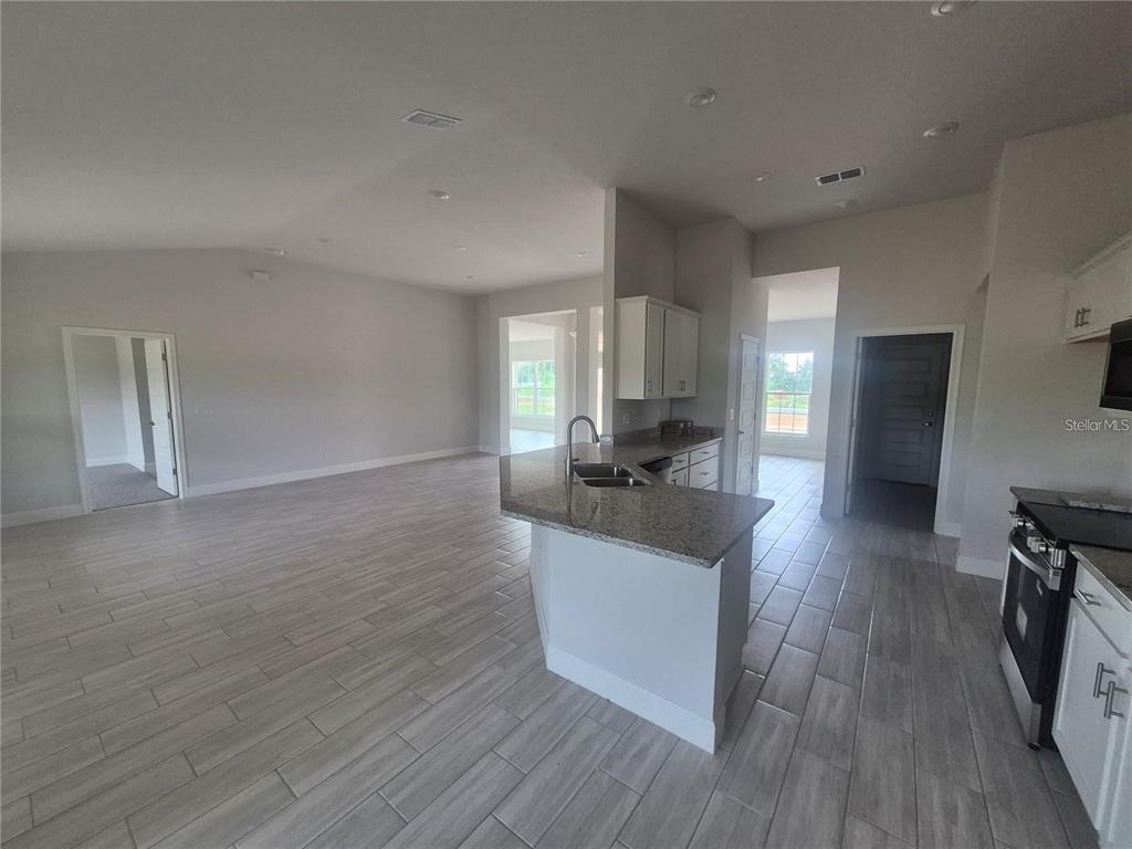 A kitchen with a granite island and light-colored tile flooring opens into a living area — 36861 HIDDEN VIEW CIRCLE, DADE CITY, FL