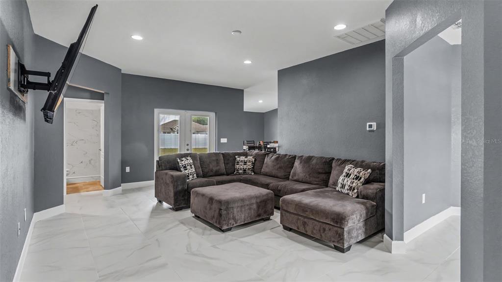 A living room with gray walls, white tile flooring, and a large dark sectional sofa — 2048 WINDING RIVER COVE, BARTOW, FL