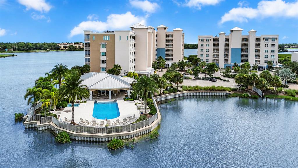 An aerial view shows a multi-story apartment complex with a pool deck overlooking a lake — 10530 BOARDWALK LOOP UNIT 304, BRADENTON, FL