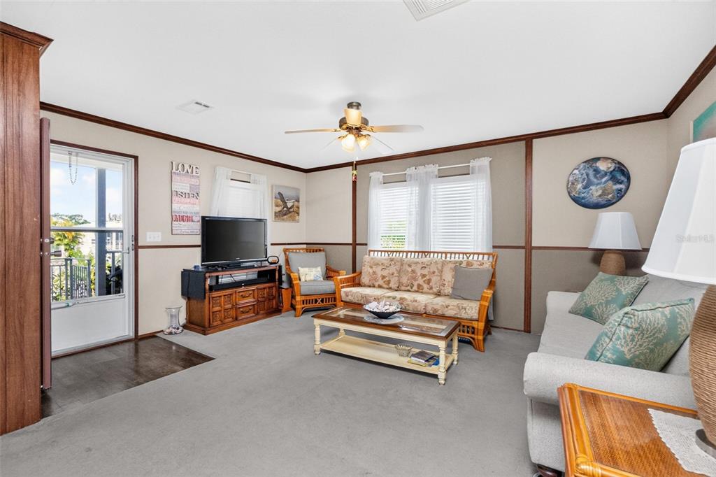A living room with gray carpet, a ceiling fan, a breakfast bar, and a television — 1268 SEAGULL DRIVE, ENGLEWOOD, FL