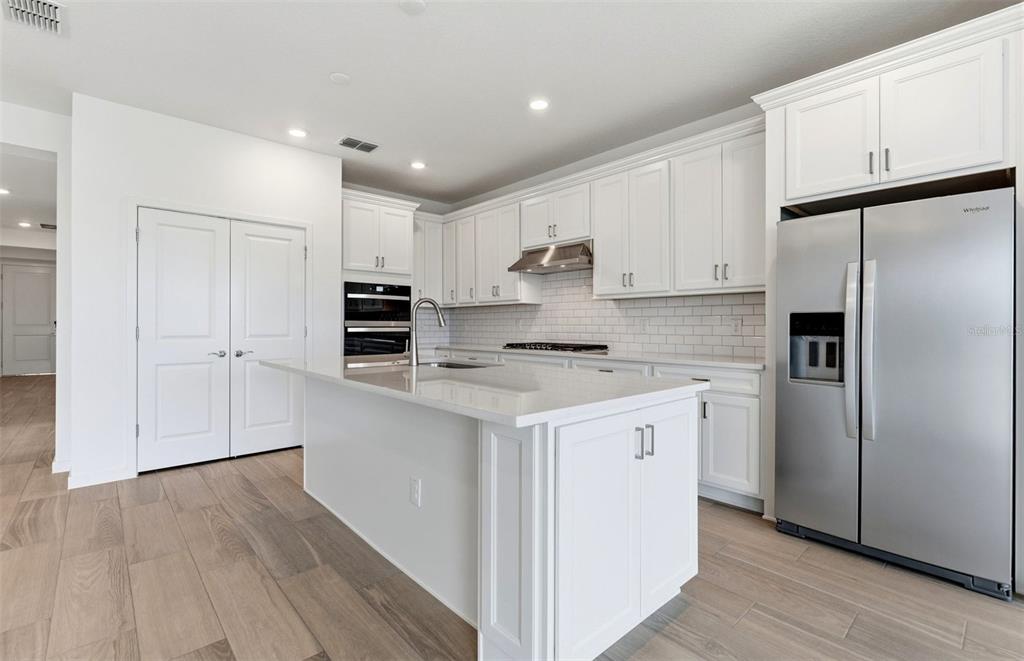 A modern kitchen features white cabinetry, stainless steel appliances, a quartz island, and wood-look flooring — 37821 CLINCH CIRCLE, ZEPHYRHILLS, FL