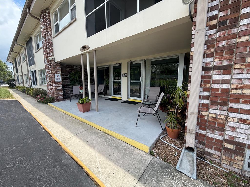 A concrete patio with chairs and potted plants sits in front of a brick building — 416 73RD AVENUE N UNIT 205, ST PETERSBURG, FL