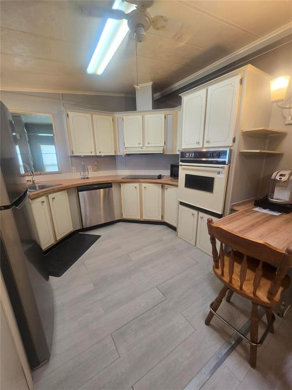 A kitchen features off-white cabinets, stainless steel appliances, wood-look flooring, and a small wooden table — 4645 BURNEY DRIVE, HOLIDAY, FL