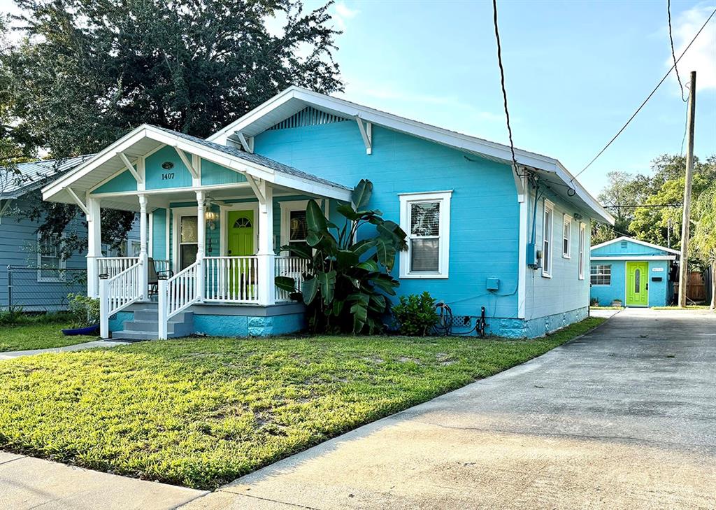 A bright blue bungalow features a white front porch, a lime green door, and a driveway — 1407 E RIDGEWOOD STREET, ORLANDO, FL