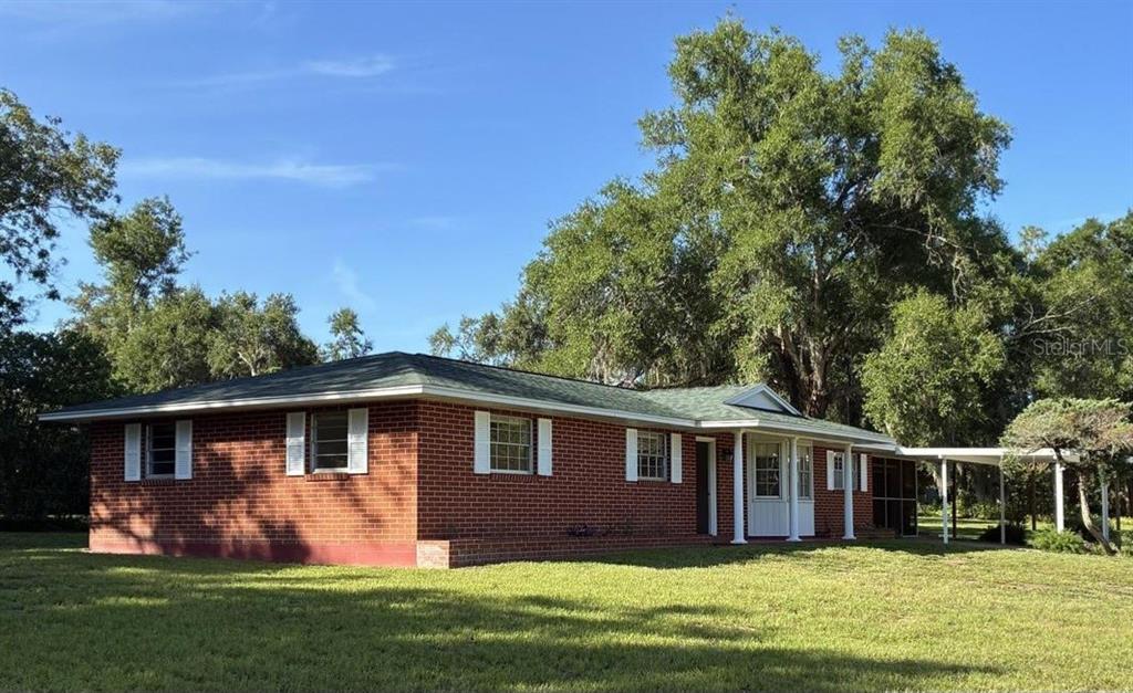 A single-story red brick house with white shutters, a green roof, and a side carport — 4926 MAGNOLIA RIDGE ROAD, FRUITLAND PARK, FL