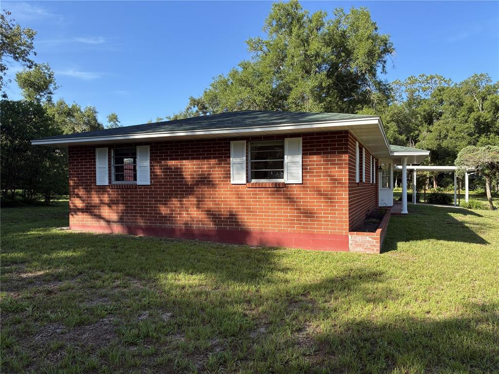 A covered concrete patio features a brick wall, a white door, and a screened enclosure — 4926 MAGNOLIA RIDGE ROAD, FRUITLAND PARK, FL