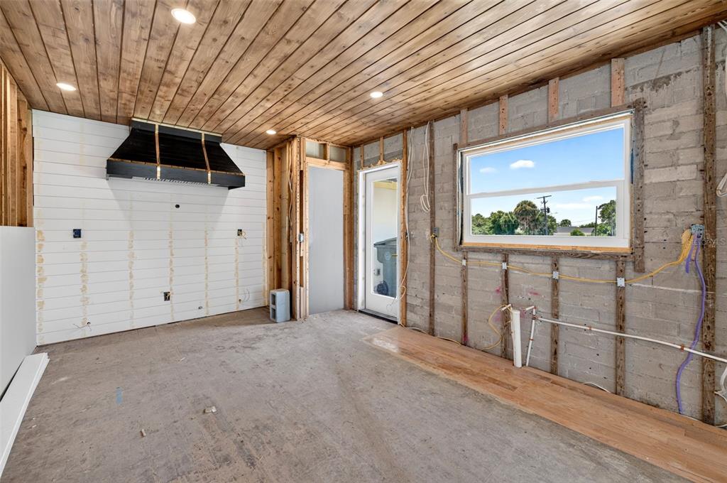 An unfinished kitchen features a wood-paneled ceiling, a black range hood, and exposed concrete walls — 2314 S PENINSULA DRIVE, DAYTONA BEACH, FL