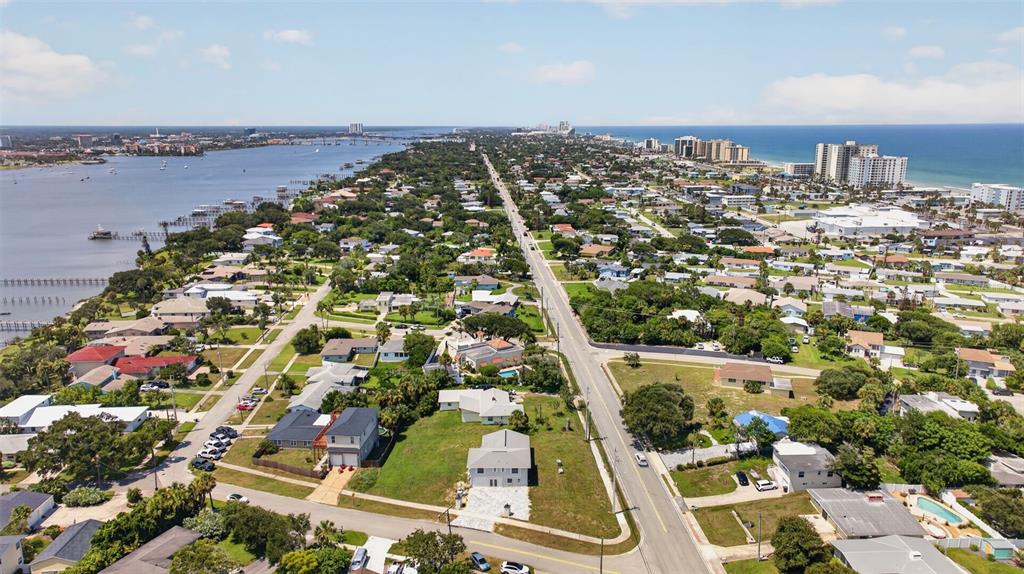 An aerial view shows a coastal neighborhood with houses, a main road, and nearby water — 2314 S PENINSULA DRIVE, DAYTONA BEACH, FL