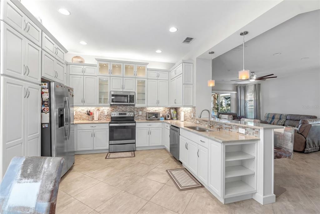 A kitchen with white cabinetry, stainless steel appliances, and a peninsula overlooking a living area — 4912 SANDY GLEN WAY, WIMAUMA, FL