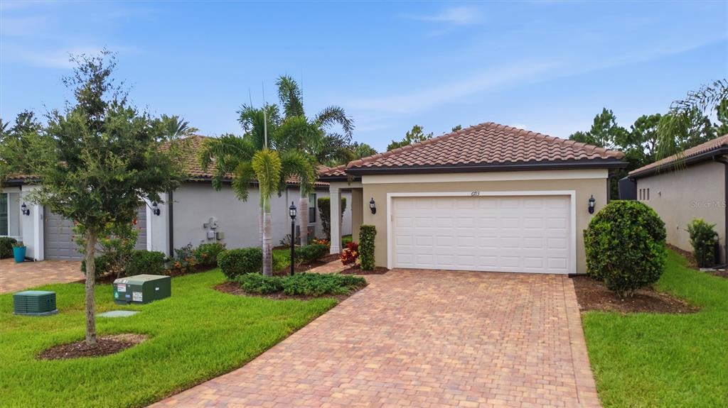 A single-story house with a tan exterior, a two-car garage, and a brick paver driveway — 6713 ALSTEAD CIRCLE, BRADENTON, FL