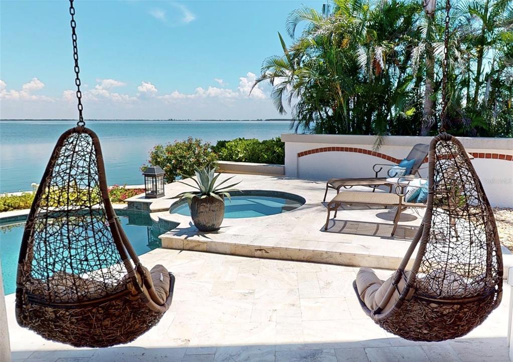 A patio with two hanging chairs, a small pool, and a hot tub overlooking the water — 101 9TH STREET E, TIERRA VERDE, FL