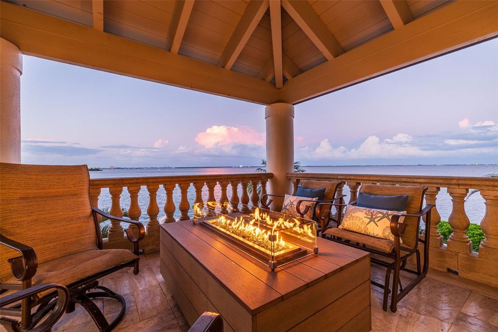 A covered balcony features a rectangular fire pit table, patio chairs, and a stone balustrade railing — 101 9TH STREET E, TIERRA VERDE, FL