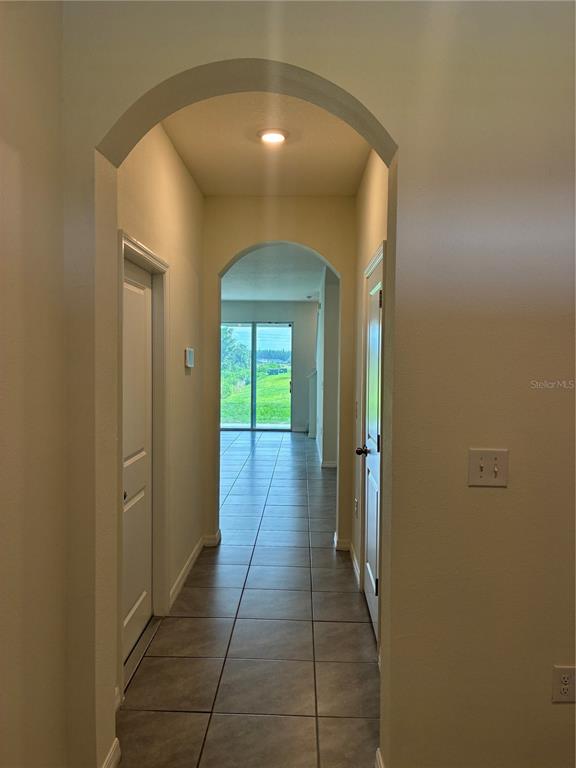 A tiled hallway with arched entryways leads to a room with sliding glass doors — 34218 REDWOOD DAWN LANE, WESLEY CHAPEL, FL