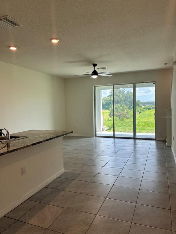 A kitchen island with granite countertops overlooks a tiled living area with sliding glass doors — 34218 REDWOOD DAWN LANE, WESLEY CHAPEL, FL