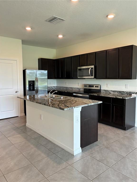 A kitchen features dark wood cabinets, granite countertops, stainless steel appliances, and light tile flooring — 34218 REDWOOD DAWN LANE, WESLEY CHAPEL, FL