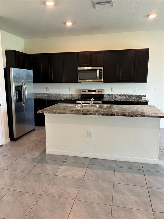 A kitchen features dark wood cabinets, stainless steel appliances, and a granite-topped island — 34218 REDWOOD DAWN LANE, WESLEY CHAPEL, FL