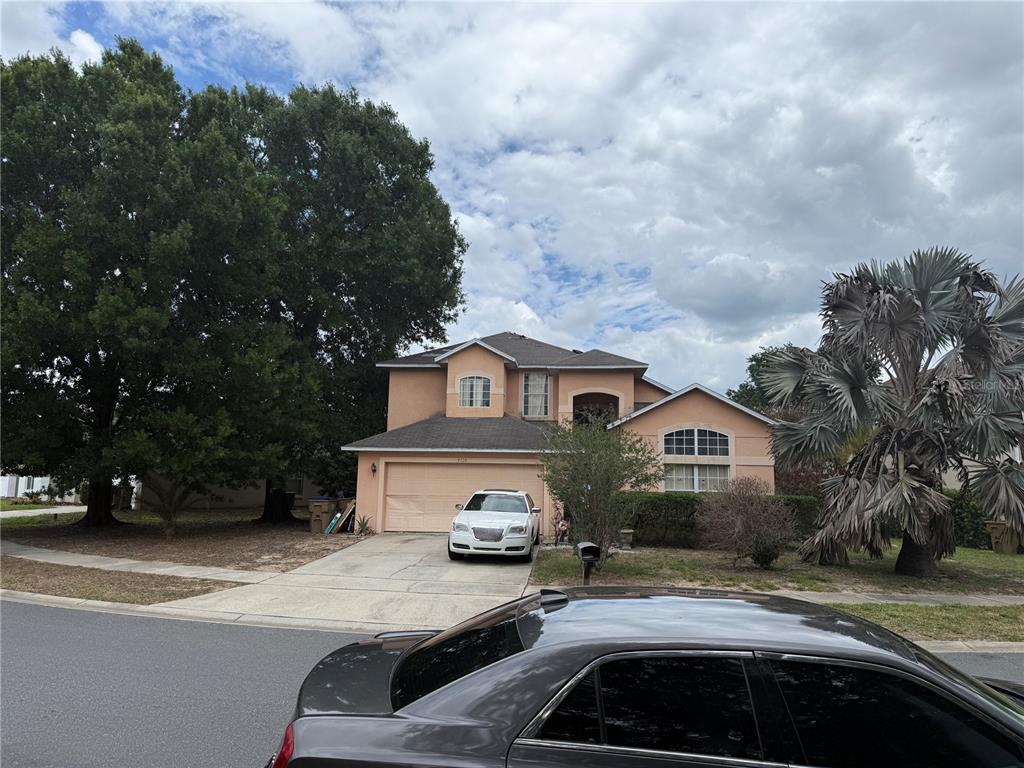 A two-story suburban house with a tan stucco exterior, a two-car garage, and a driveway — 8128 YELLOW CRANE DRIVE, KISSIMMEE, FL