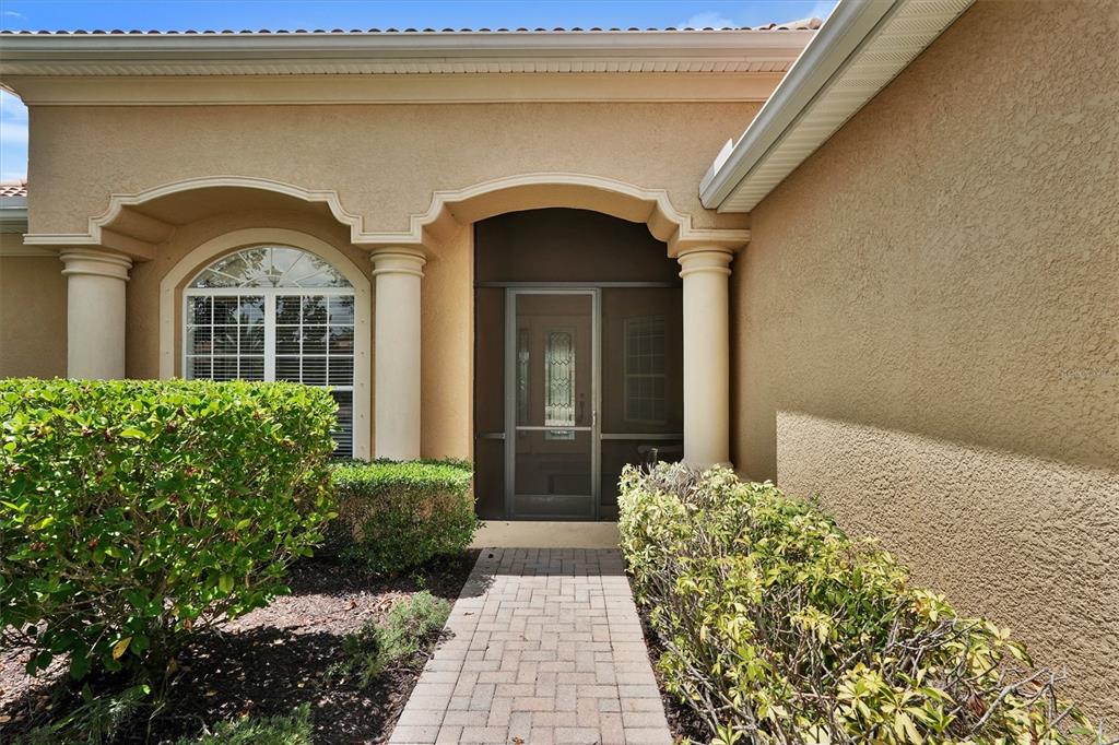 A paved walkway leads to a covered entryway with columns and a screened front door — 7910 RIVER PRESERVE DRIVE, BRADENTON, FL
