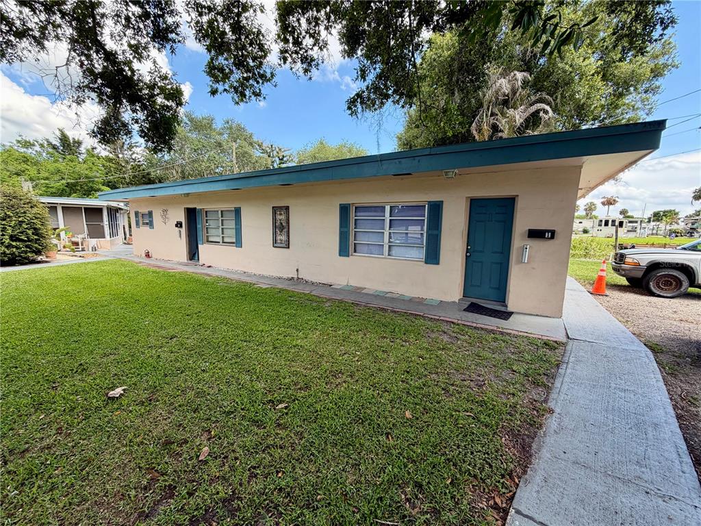 A single-story tan building with a blue door and shutters sits beside a grassy lawn — 3112 SE 29TH TERRACE, OKEECHOBEE, FL