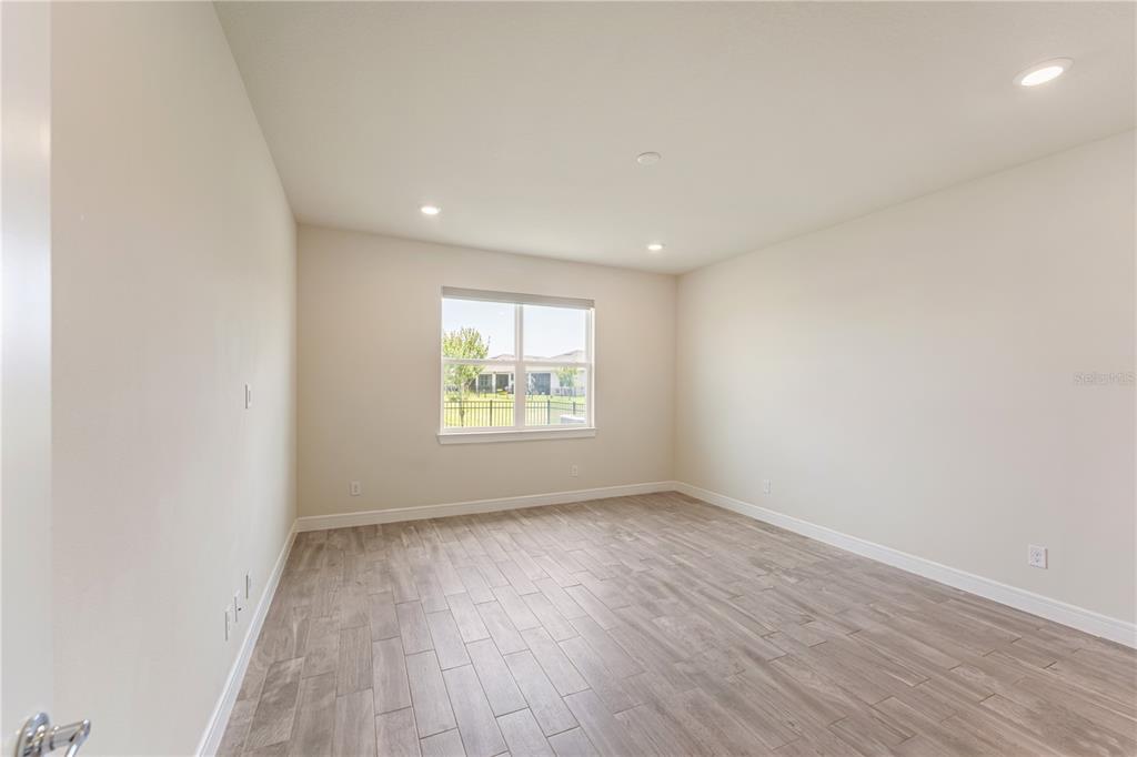 An empty bedroom features light-colored walls, recessed lighting, and wood-look tile flooring — 1994 SPRING SHOWER CIRCLE, KISSIMMEE, FL