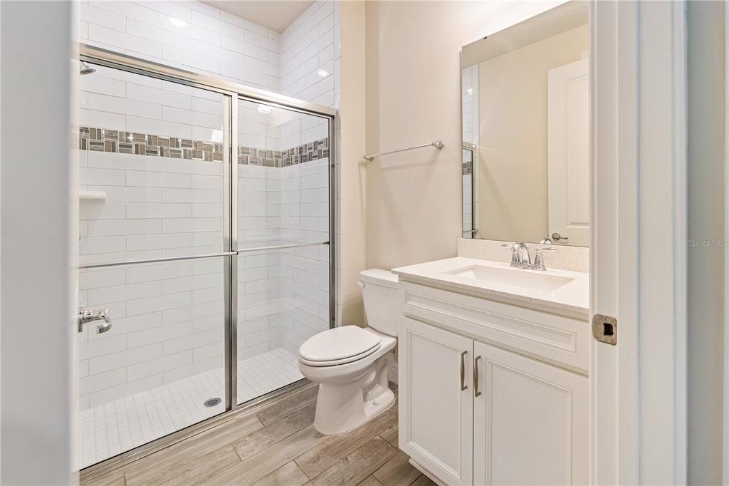 A bathroom with a glass-enclosed shower, white vanity, toilet, and wood-look tile flooring — 1994 SPRING SHOWER CIRCLE, KISSIMMEE, FL