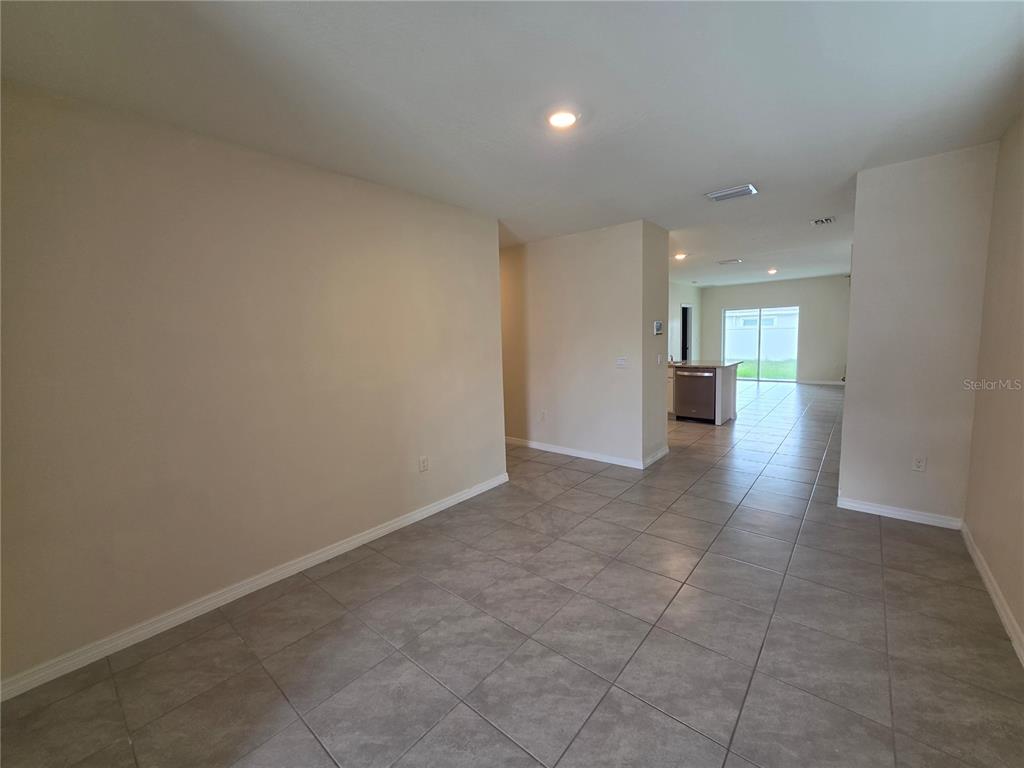 An open-concept living area features beige walls, tile flooring, and a view into the kitchen — 17007 BLISTER WING DRIVE, WIMAUMA, FL