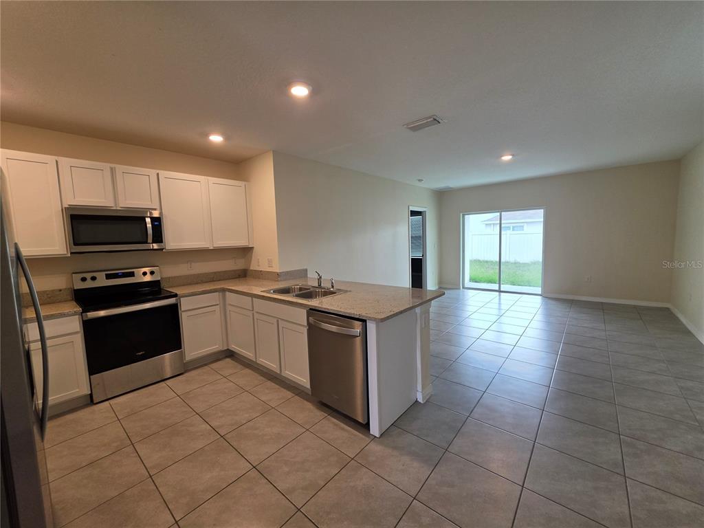 A kitchen with white cabinets, stainless steel appliances, and tile flooring opens to a living area — 17007 BLISTER WING DRIVE, WIMAUMA, FL