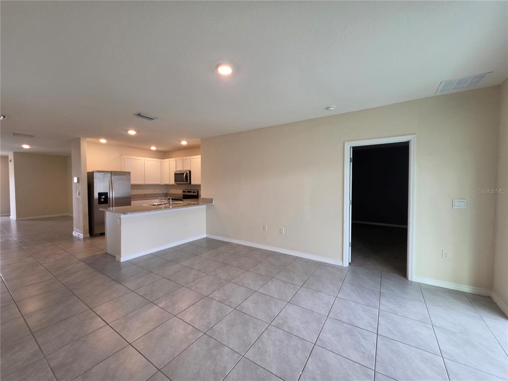An open-concept living area features light tile flooring, a kitchen with white cabinets, and stainless appliances — 17007 BLISTER WING DRIVE, WIMAUMA, FL