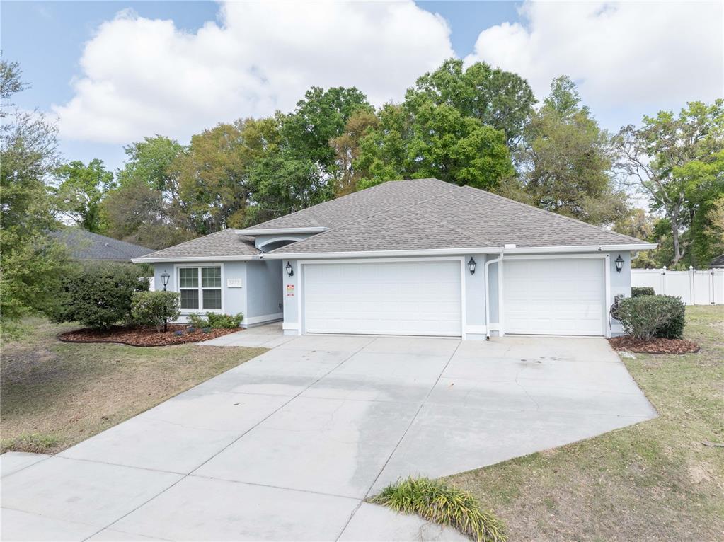 A single-story house with a light blue exterior, a three-car garage, and a concrete driveway — 5273 SW 96TH PLACE, OCALA, FL