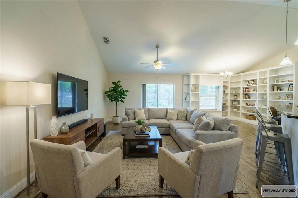 A virtually staged living room features a sectional sofa, two armchairs, and built-in wall shelving — 5273 SW 96TH PLACE, OCALA, FL