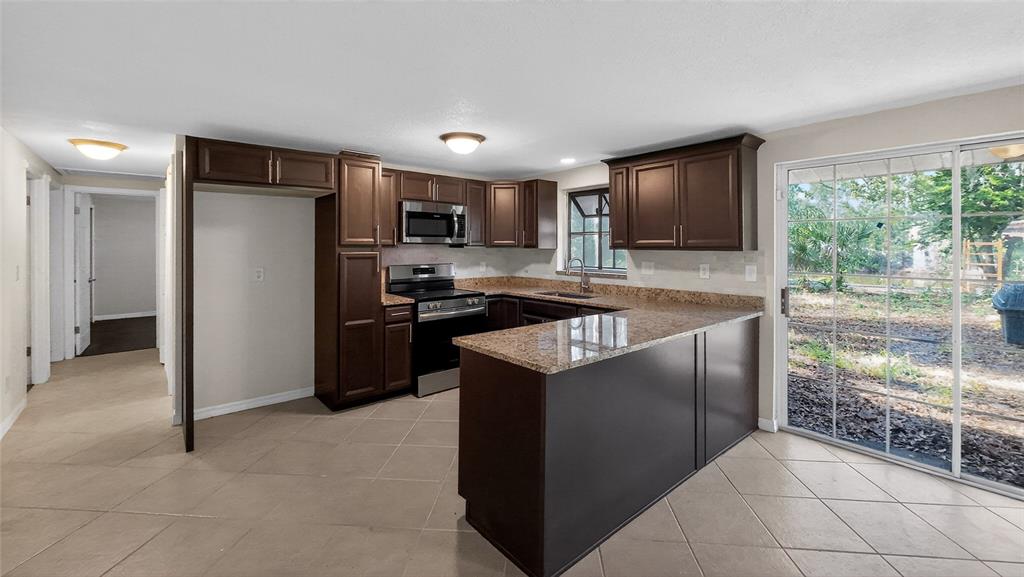 A kitchen features dark wood cabinets, granite countertops, stainless steel appliances, and a sliding glass door — 17220 ESTES ROAD, LUTZ, FL