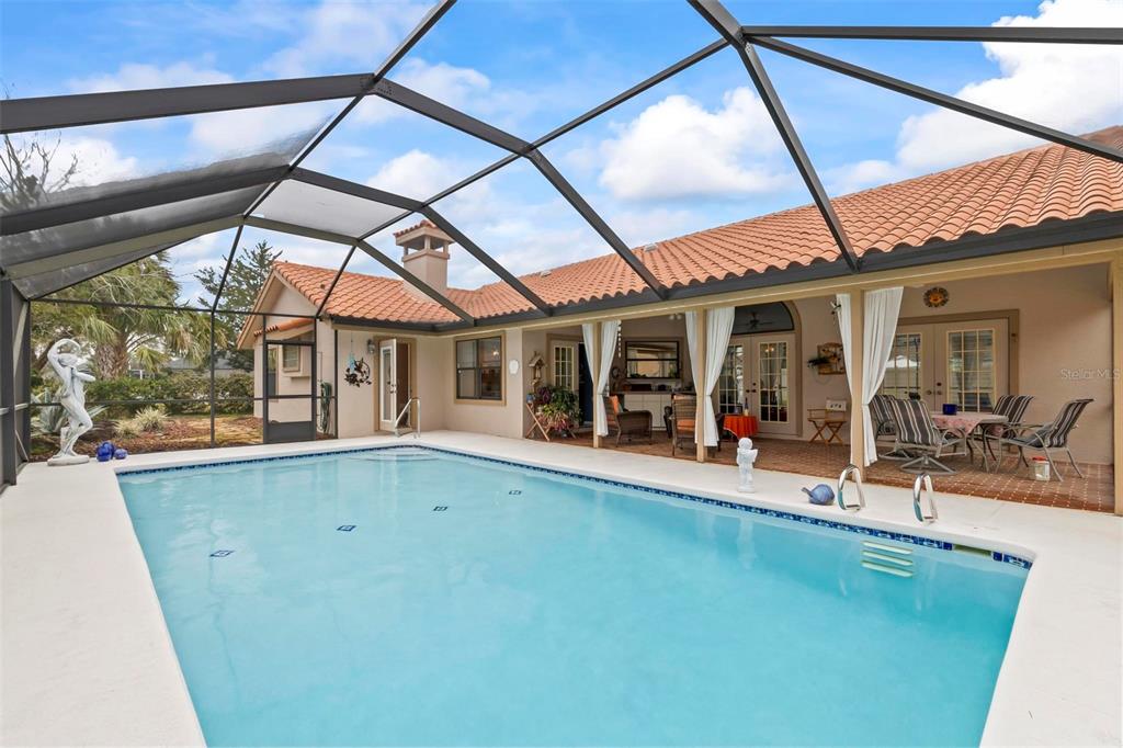 A swimming pool with a screened enclosure sits on a patio next to a house — 130 BAYSIDE DRIVE, PALM COAST, FL
