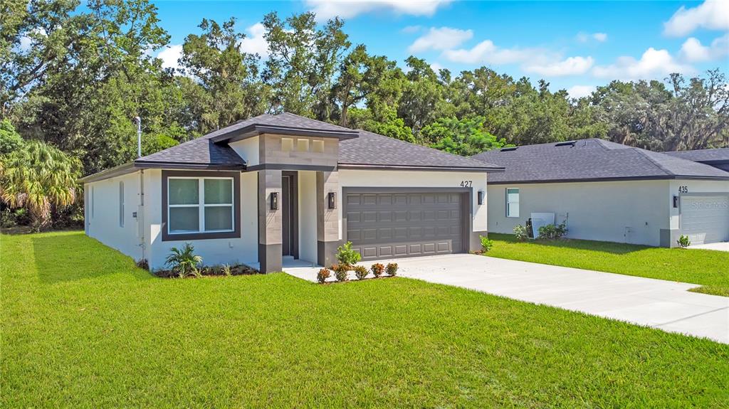 A single-story house with a gray garage, white stucco walls, and a dark shingled roof — 427 E 13TH STREET, APOPKA, FL