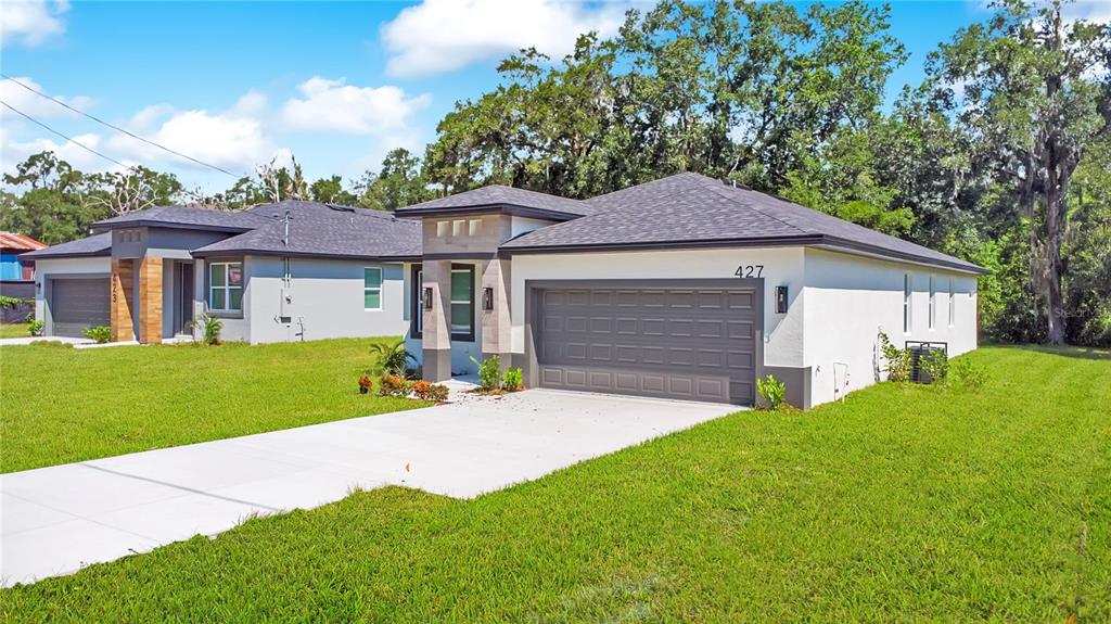 A modern single-story house with a gray garage and white stucco exterior sits on grass — 427 E 13TH STREET, APOPKA, FL