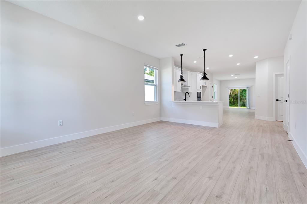 An open-concept living area features light wood-look flooring, white walls, and a kitchen island — 427 E 13TH STREET, APOPKA, FL