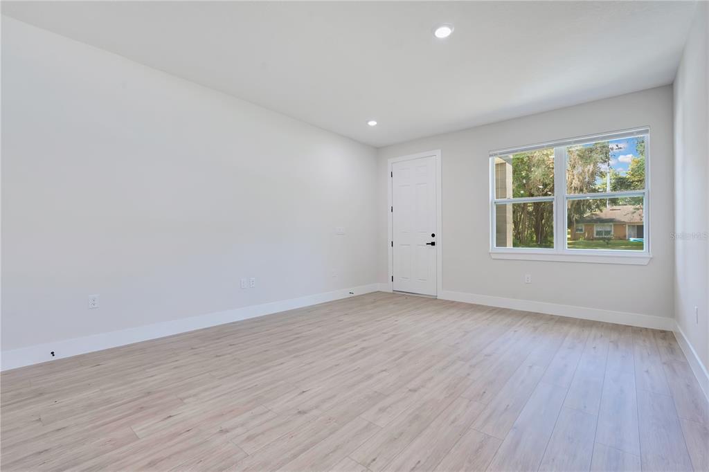 An empty room with light wood-look flooring, white walls, a white door, and a window — 427 E 13TH STREET, APOPKA, FL